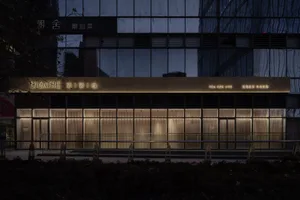 A modern Asian building at night with a large glass front reflecting the surrounding environment and several windows on each side