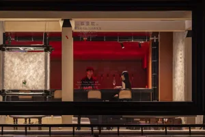 A casual bar scene with a modern design, featuring a red accent wall, a counter, and chairs, with patrons enjoying drinks and conversation