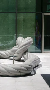 A minimalist space with a large rope chair in front of a glass wall, illuminated by sunlight