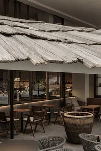 An open-air restaurant with wooden tables and chairs, surrounded by plants and natural elements, in a warm and inviting atmosphere with bright daytime lighting