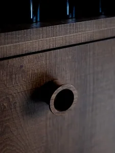 A wooden cabinet with a drawer featuring a hole in the middle, part of a larger piece of furniture with a traditional design