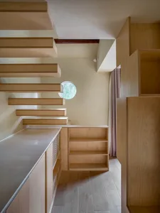 Open living area with wooden cabinets, a sink, and a dining table surrounded by chairs, illuminated by natural light