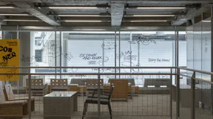 Modern restaurant with wood and glass elements, chairs, and a large window allowing natural light