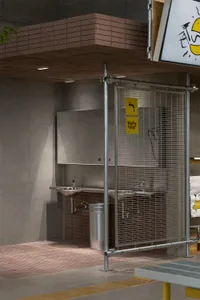 Industrial bathroom with metal fencing, two sinks, and a trash can, giving off a utilitarian and functional vibe