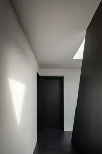 A simple hallway with a black door and a white wall, creating a striking contrast