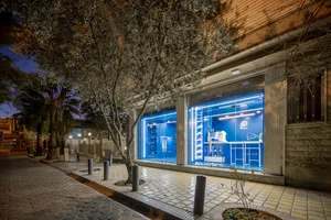 Well-lit storefront with a brick facade, large window display, and potted plants, featuring two benches near the entrance