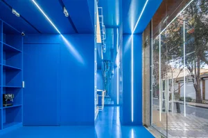 A bright blue hallway with reflective surfaces, concrete walls, and two doors, conveying a sense of openness and simplicity