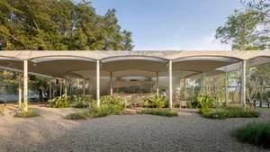 An open-air restaurant with a relaxed atmosphere, featuring dining tables and chairs surrounded by trees