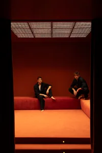 Two men sitting on a red couch in an orange room with comfortable seating and warm decor