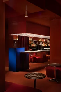 Cozy bar area with red walls, red carpet, and comfortable seating options, featuring scattered bottles and inviting atmosphere