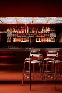 A well-stocked bar with a long orange countertop, surrounded by chairs and a selection of bottles on display