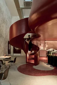 A modern staircase in a restaurant or bistro, with red metal stairs, chairs, and an inviting atmosphere