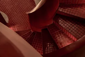 A well-lit staircase with red brick walls, wooden steps, and a metal railing, creating a warm and cozy atmosphere