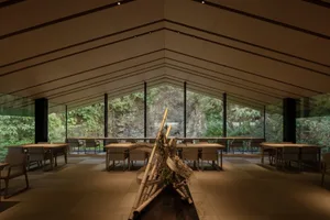 Open modern restaurant interior with tables, chairs, potted plants, and artwork on the walls
