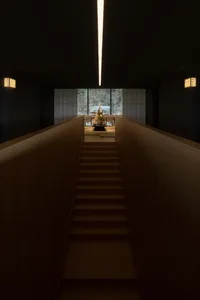 A darkened room with a wooden staircase, a statue at the bottom, and a sense of mystery and intrigue