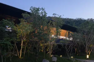 A modern building with a black exterior is surrounded by green trees, with a bench nearby, conveying a sense of tranquility and harmony between nature and architecture