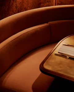 A brown leather couch and wooden dining table create a cozy seating area with two chairs and a wine glass, suggesting a space for relaxation and socializing