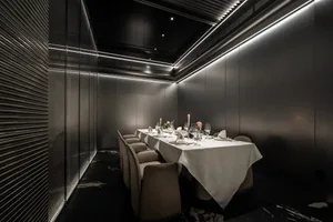 A sophisticated dining area with a long wooden table, multiple chairs, wine glasses, vases, and potted plants, perfect for special events or intimate gatherings