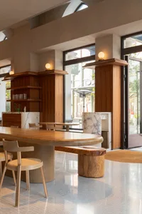 Well-lit restaurant interior with wooden tables, marble countertops, and a large window allowing natural light to enter
