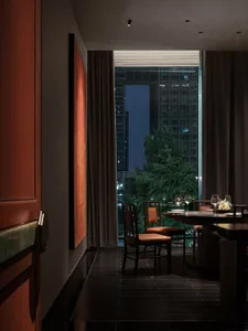 Dining area with two tables, chairs, wine glasses, and vases, illuminated by natural light through a large window