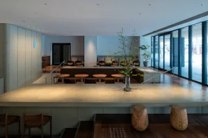 A restaurant dining area with multiple tables, chairs, and wood flooring, set against a backdrop of white and grey walls
