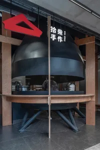 A modern Asian restaurant with a large black oven, wooden tables, and chairs, creating a warm and inviting atmosphere