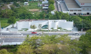 Modern museum building with a white exterior, surrounded by parked cars and a red vehicle in the center of the scene
