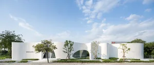 A modern building with a concrete exterior, multiple windows, and a curved design, surrounded by trees in an urban environment
