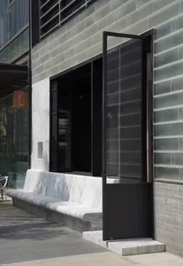 Modern building with a glass facade, a black doorway, and two concrete benches in front, set against a neutral background