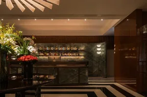 A luxurious hotel lobby bar with a marble countertop, glassware, and decorative vases, set against a neutral background