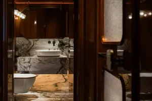 Bathroom with two sinks on a marble countertop, a wooden door, and a bowl near one sink, in a clean and organized space