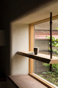 A room with a wooden shelf, a cup, and two potted plants, lit by natural light from a window