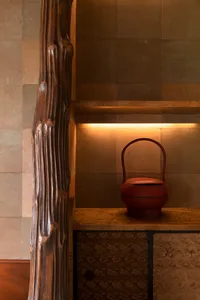 A wooden table with a red clay vase on a wall in a rustic living space