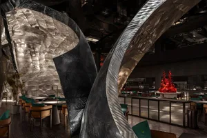 A modern restaurant interior with two large metal sculptures as centerpieces, dimly lit for an intimate ambiance
