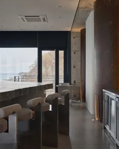 Open living area with a modern bar, chairs, a dining table, a couch, and a TV, set in a contemporary space with clean lines and minimal decoration