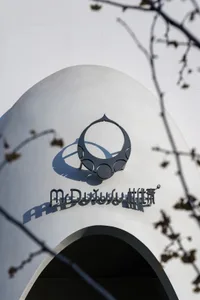 A modern building with a large white facade and a prominent circular structure on its side, set against a neutral background