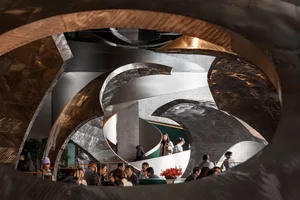A modern hotel lobby with a circular design element, metal and glass materials, and soft diffused lighting, featuring several people in the space