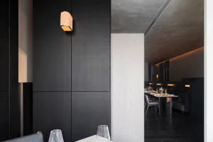 Empty restaurant dining area with a black wall, a white table, and several chairs, with a wine glass on a smaller table