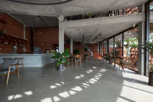 Modern restaurant interior with a large cement wall, concrete floor, and potted plants, featuring a minimalist and functional atmosphere