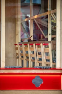 A restaurant interior with wooden tables and red table tops, sixteen chairs, and a cozy atmosphere