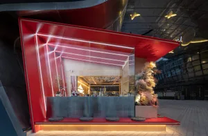 A modern bar area with a red wall, sleek design, and greenery, featuring a countertop, bottles, cups, and bowls