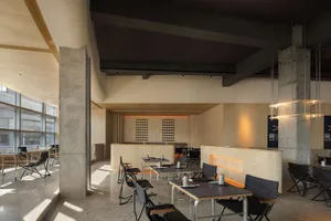 A modern restaurant interior with multiple dining tables and chairs, white and grey walls, and warm lighting