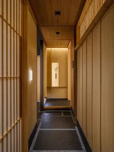 Narrow hallway with wooden walls and floors, featuring two doors and a dark atmosphere due to lack of natural light