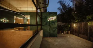 Cozy bistro interior with green tile walls, two dining tables, and a potted plant adding to the ambiance