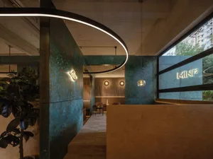 A cozy restaurant interior with green and brown tones, featuring two dining tables, chairs, and potted plants