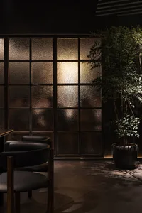 Dimly lit room with a black chair in front of a glass door, allowing natural light to enter and illuminate the space