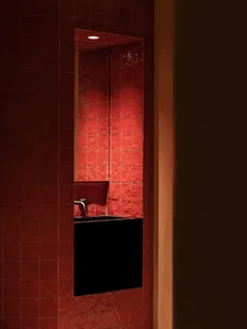 Bathroom with red tiles on the walls and floor, a black sink, and warm lighting
