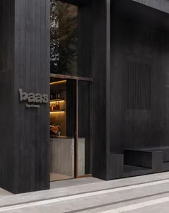 Modern bar entrance with a black doorway, a sign reading BAAS, and a well-stocked bar area with bottles on surfaces