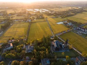 Aerial view of a farm field with trees and a church building in the distance, set in a peaceful countryside atmosphere