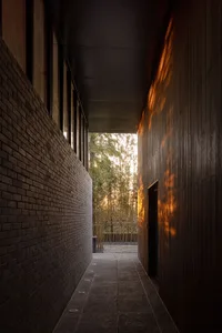 A serene courtyard entrance with a brick wall, a wooden doorway, and trees in the background